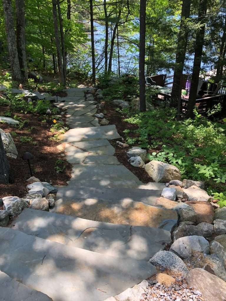 Natural stone staircase and woodland pathway leading to a lakefront property by Landscapes by Tom in New Hampshire