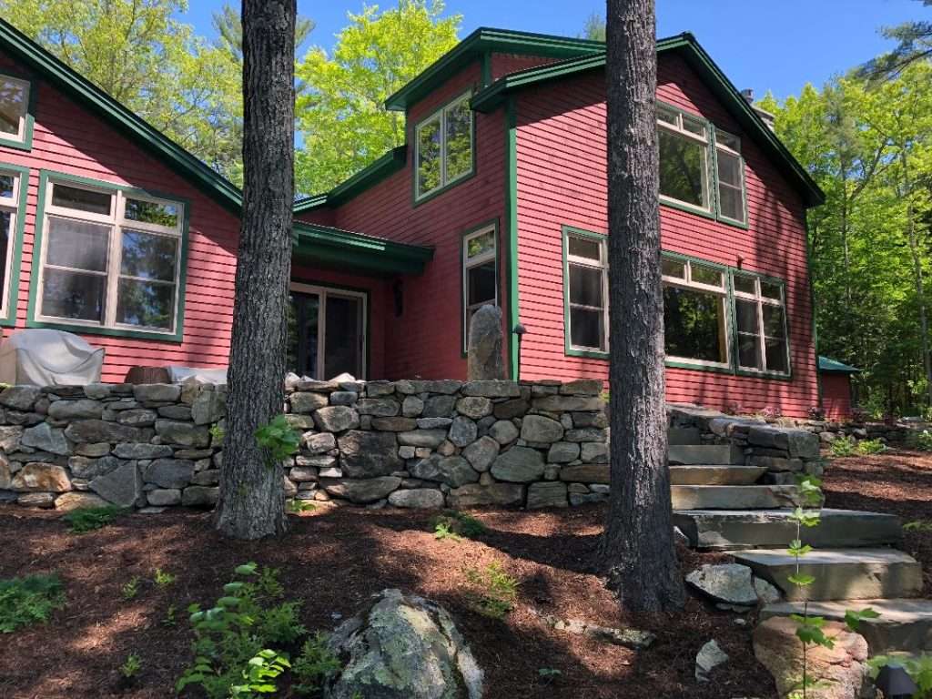 Natural stone retaining wall and granite staircase installation for a woodland New Hampshire home by Landscapes by Tom