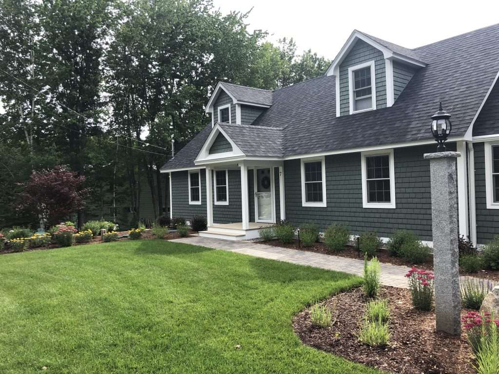 Front yard landscape and walkway installation featuring paver front walk, foundation shrubs, flowering perennial gardens, ornamental grasses, and professionally maintained lawn at a New Hampshire home