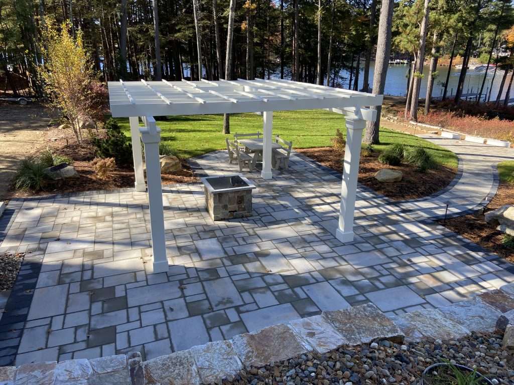 Multi-level granite staircase and natural stone retaining wall installation with custom paver walkways, boulder accents, and professionally designed hillside landscaping for a New Hampshire lakeside property