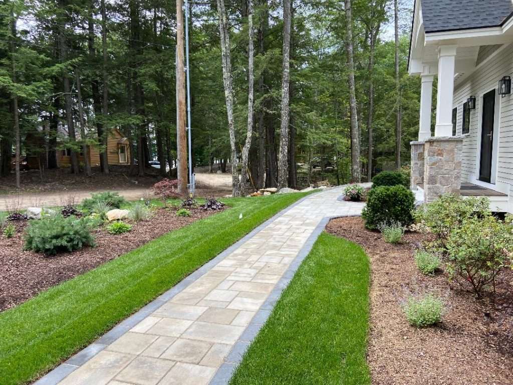 Custom paver patio and landscape installation featuring granite accents, natural stone retaining walls, outdoor living space, landscape lighting, and professionally designed planting beds for a beautiful New Hampshire backyard retreat