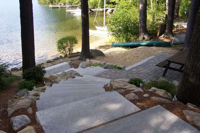 Completed lakeside permeable paver patio with custom granite steps, shoreline landscaping, and waterfront outdoor living design by Landscapes by Tom in New Hampshire
