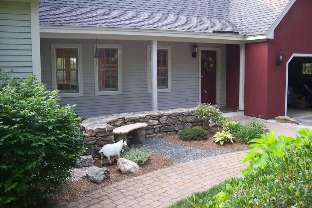 Completed front entry planting bed renovation with professional landscaping and natural stone accents by Landscapes by Tom in New Hampshire