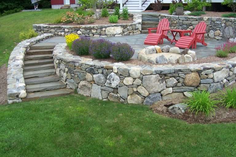 Outdoor living landscape design featuring custom paver patios, natural stone retaining walls, fire pit gathering spaces, outdoor kitchens, granite steps, and professionally designed backyard entertaining areas for New Hampshire homes