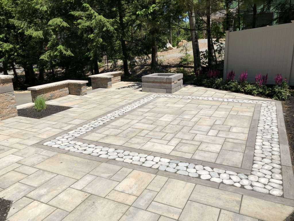 Custom paver patio with decorative river rock inlay, modern fire pit, geometric hardscape design, and landscaped garden beds for a stylish backyard outdoor living space 4