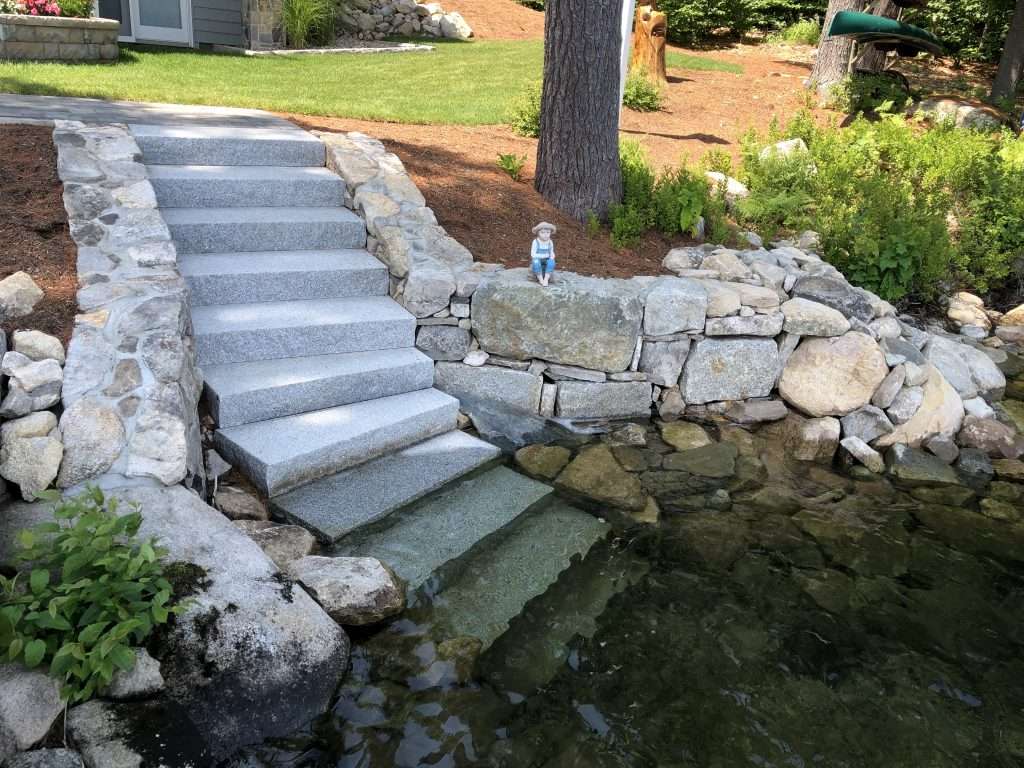 Custom granite lake access stairs with natural stone retaining wall and shoreline stabilization designed for a New Hampshire waterfront property