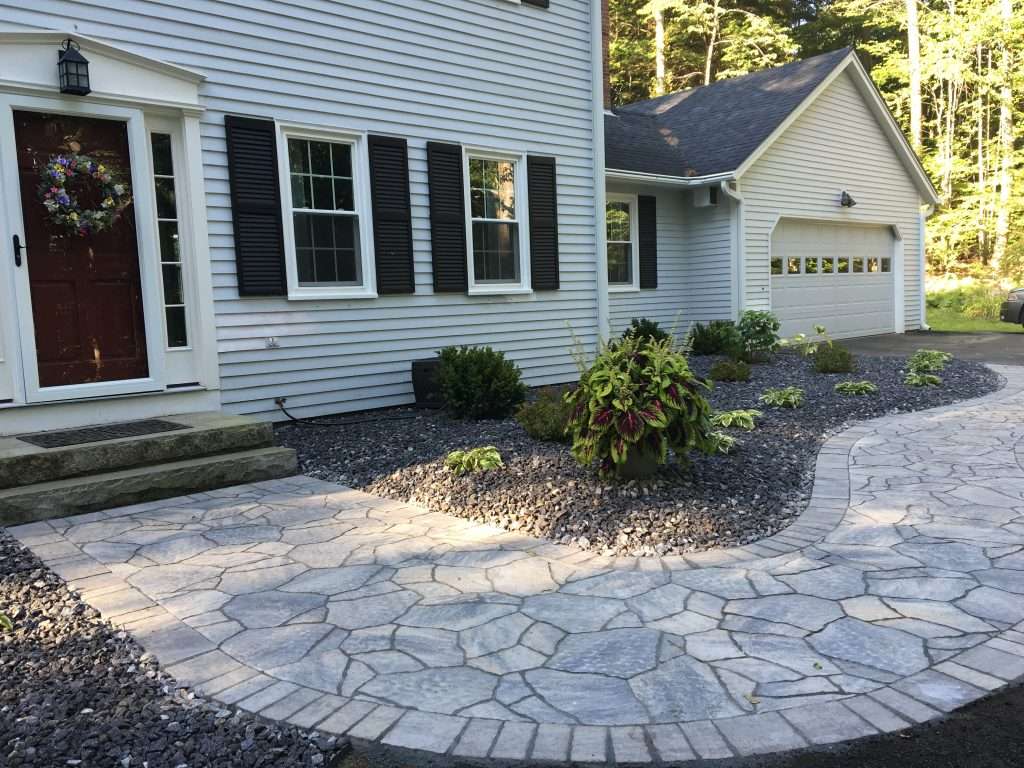 Low Maintenance Gardens 1 Custom natural stone walkway and front entry landscaping featuring curved hardscape design, decorative river rock beds, granite front steps, foundation plantings, and professionally crafted curb appeal enhancements for a New Hampshire home