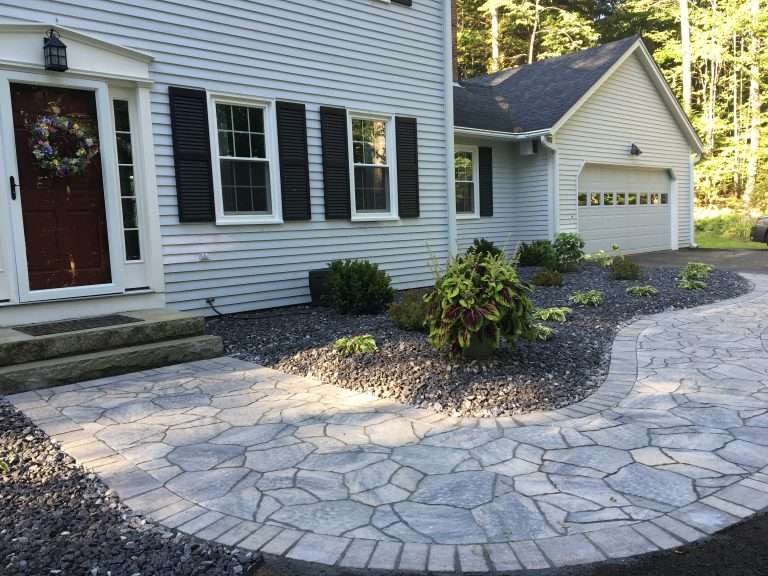 Custom natural stone walkway and front entry landscaping featuring curved hardscape design, decorative river rock beds, granite front steps, foundation plantings, and professionally crafted curb appeal enhancements for a New Hampshire home