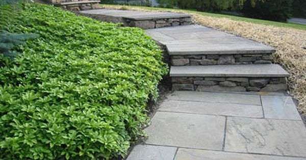 Natural stone walkway installation with professionally designed garden beds, fresh mulch, ornamental plantings, and elegant residential landscaping for a New Hampshire home