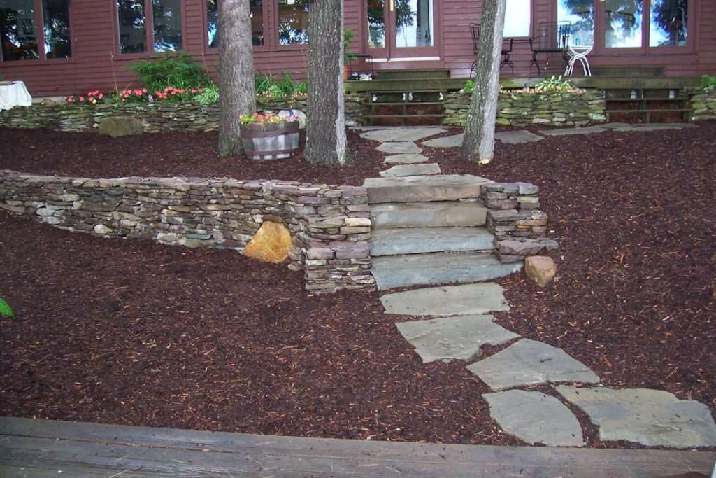 Natural stone walkway and handcrafted granite steps with rustic retaining wall terraces designed for a sloped New Hampshire lakeside property